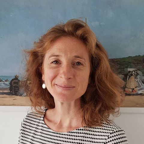 Olivia Luquet, souriante, cheveux roux mi-longs, devant une peinture de bord de mer